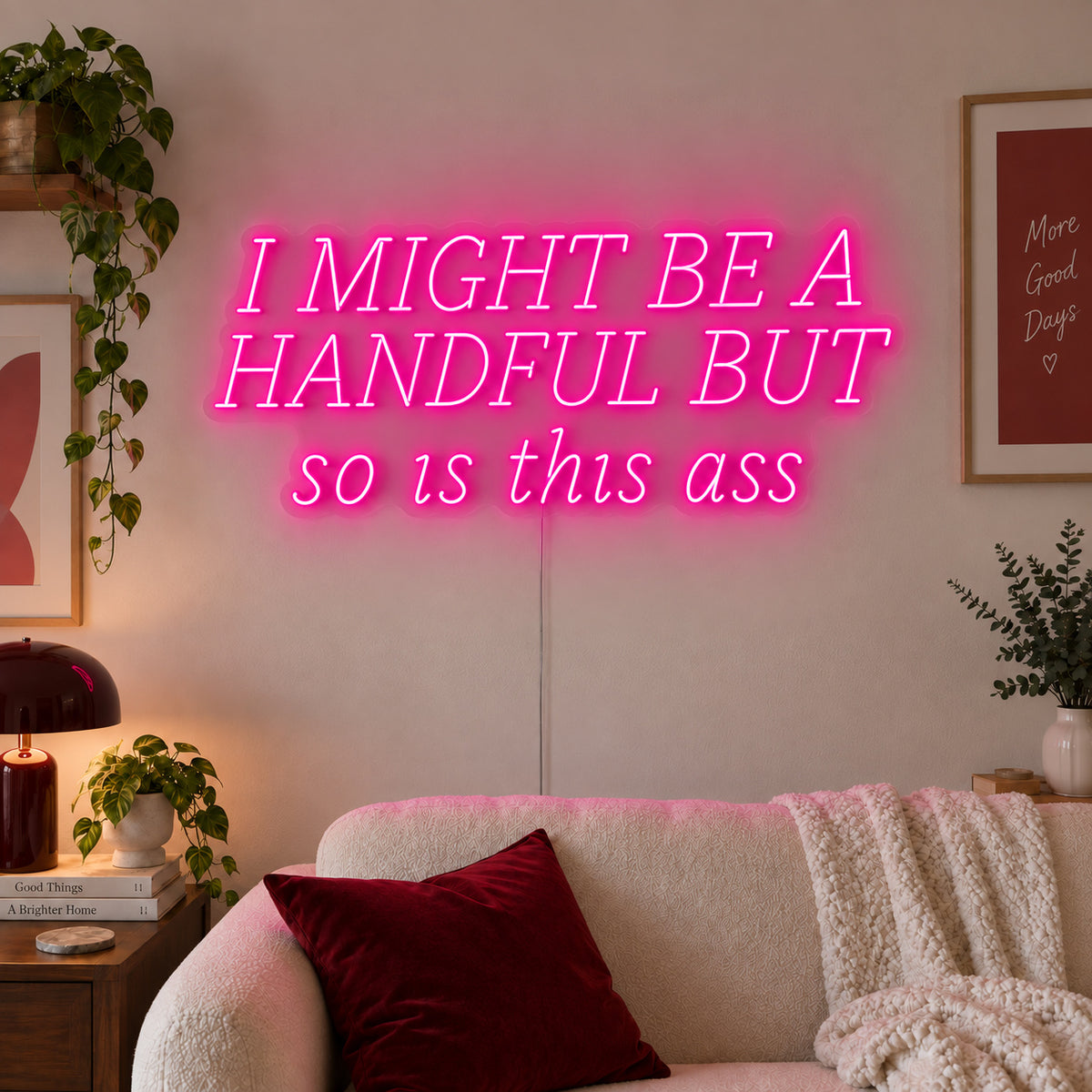 Rose Red version of the I Might Be A Handful But So Is This Ass Neon Sign, shown in wide lettering above a cream sofa.