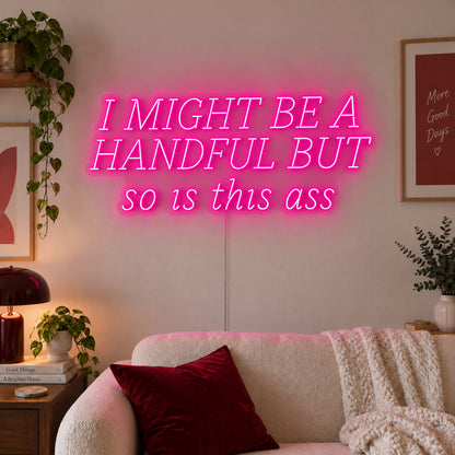 Rose Red version of the I Might Be A Handful But So Is This Ass Neon Sign, shown in wide lettering above a cream sofa.