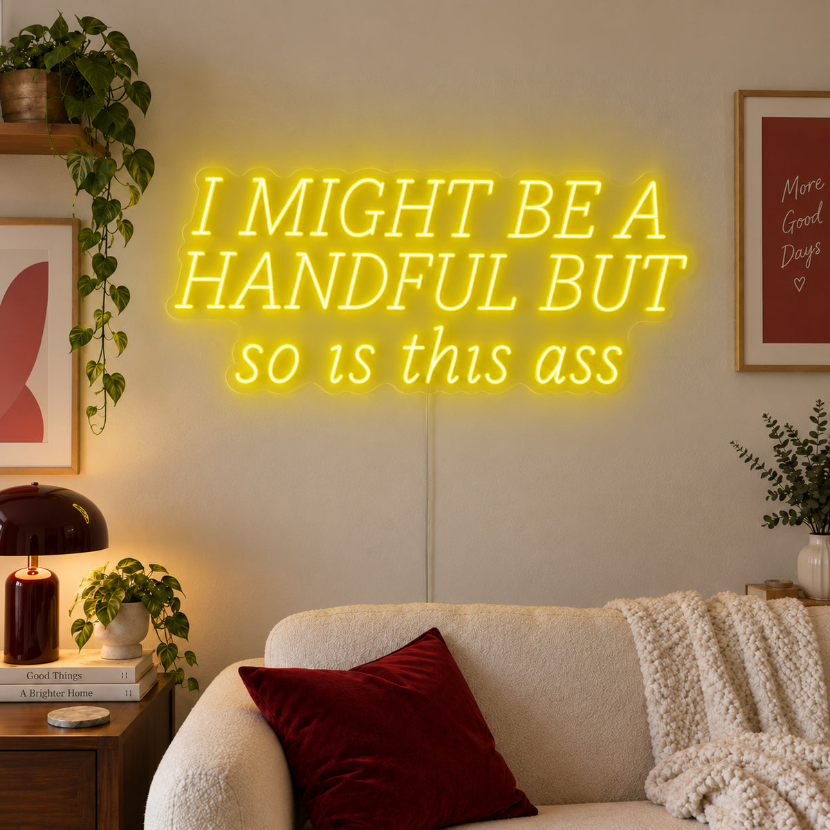I Might Be A Handful But So Is This Ass Neon Sign with yellow lighting, displayed in wide lettering above a cream sofa.