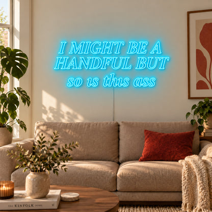 Ice Blue version of the I Might Be A Handful But So Is This Ass Neon Sign, shown in compact lettering above a cream sofa.