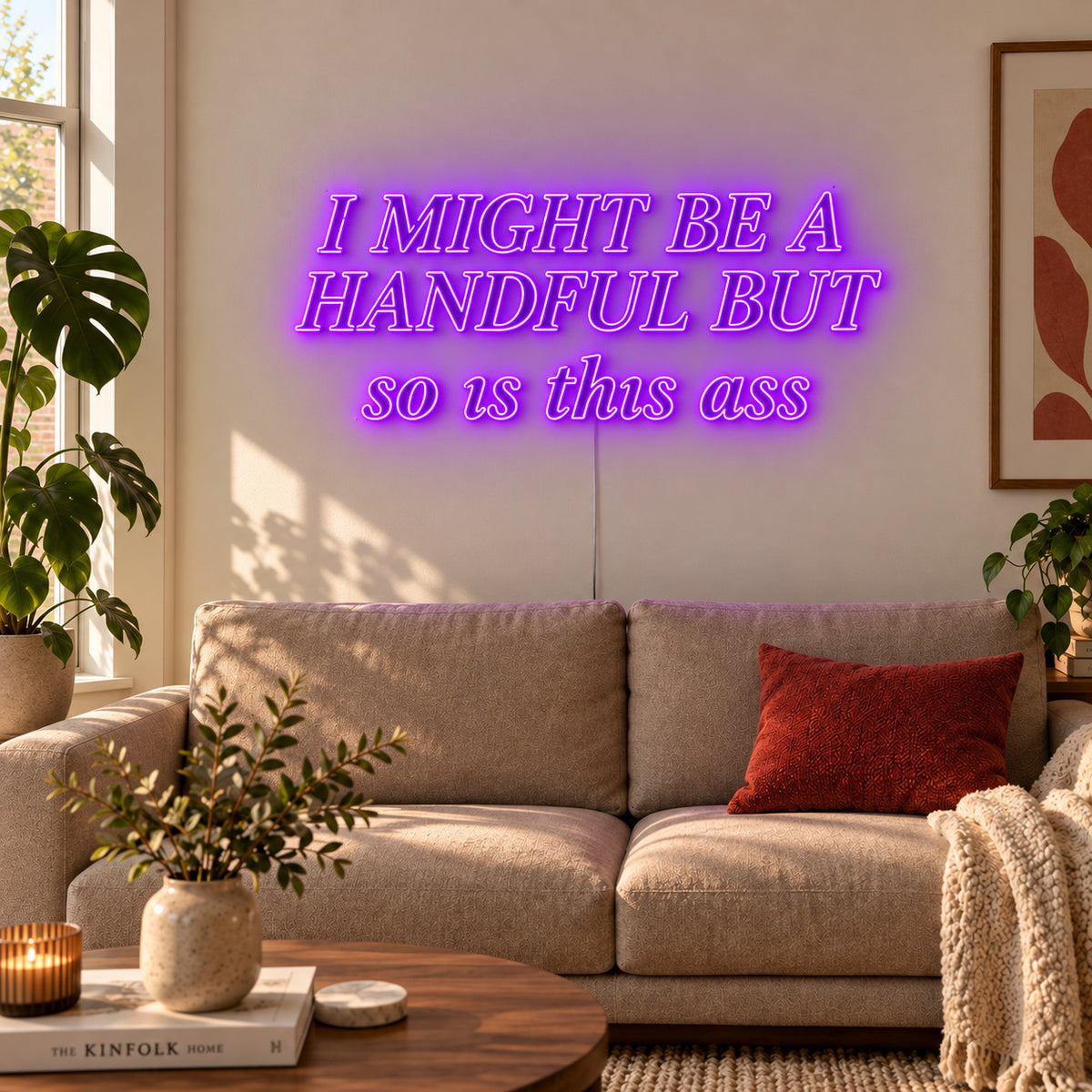 I Might Be A Handful But So Is This Ass Neon Sign with purple lighting, displayed in compact lettering above a cream sofa.