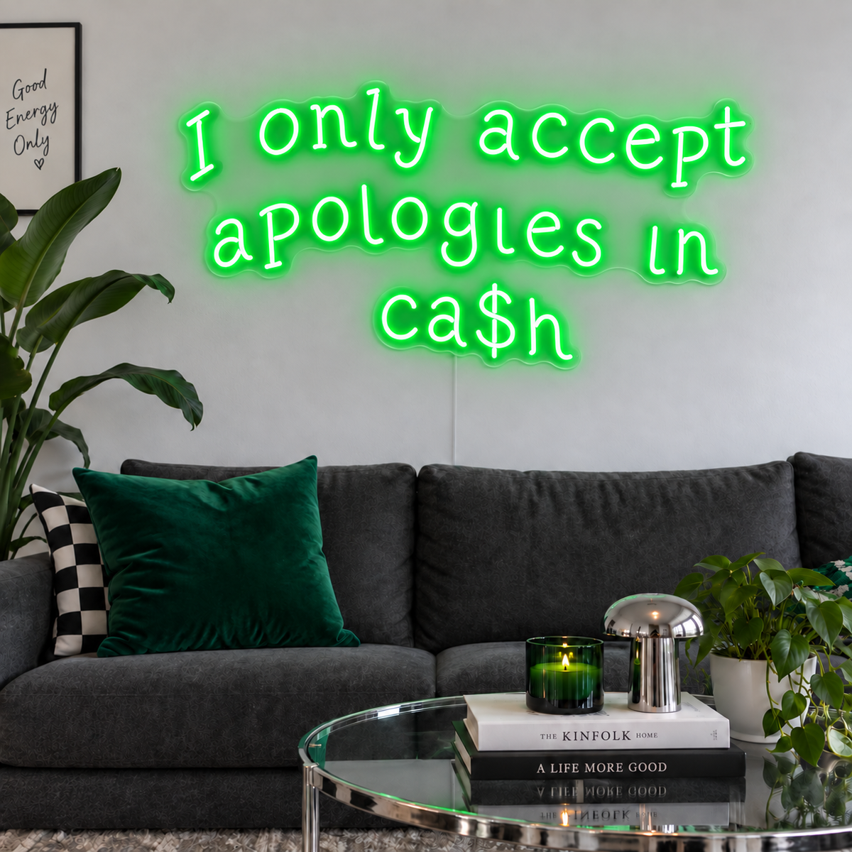 I Only Accept Apologies In Ca$h Neon Sign in green above a charcoal sofa with green cushions.