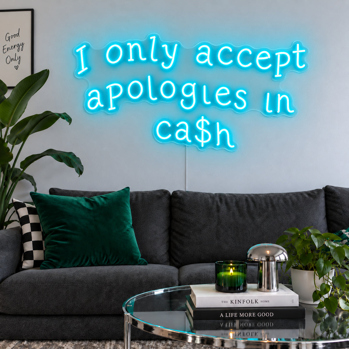 Ice Blue version of the I Only Accept Apologies In Ca$h Neon Sign, shown above a charcoal sofa with green cushions.