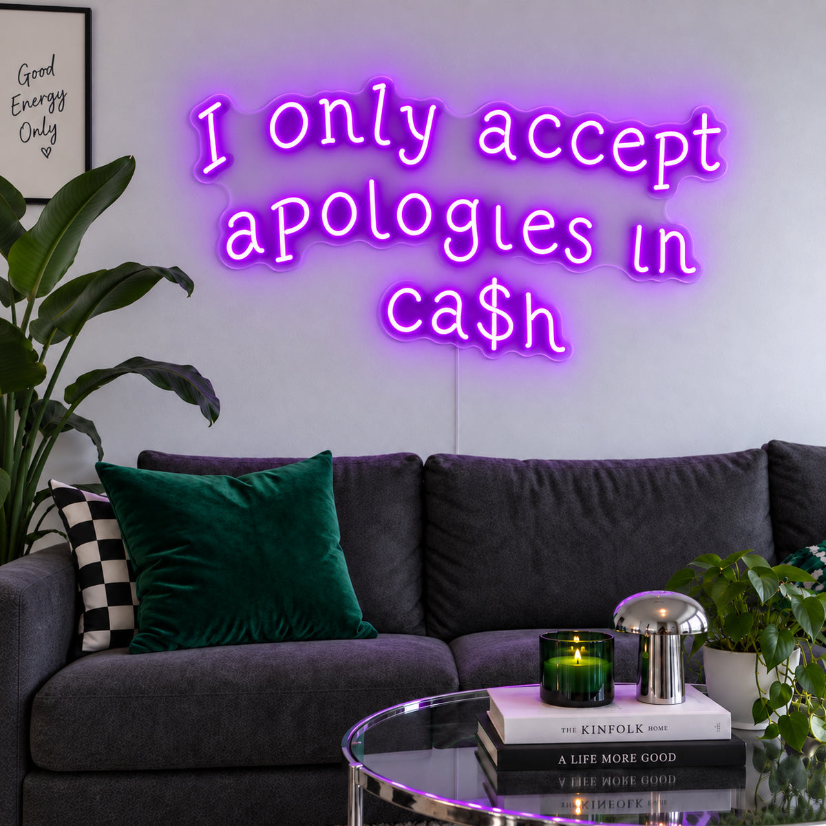 I Only Accept Apologies In Ca$h Neon Sign with purple lighting, displayed above a charcoal sofa with green cushions.