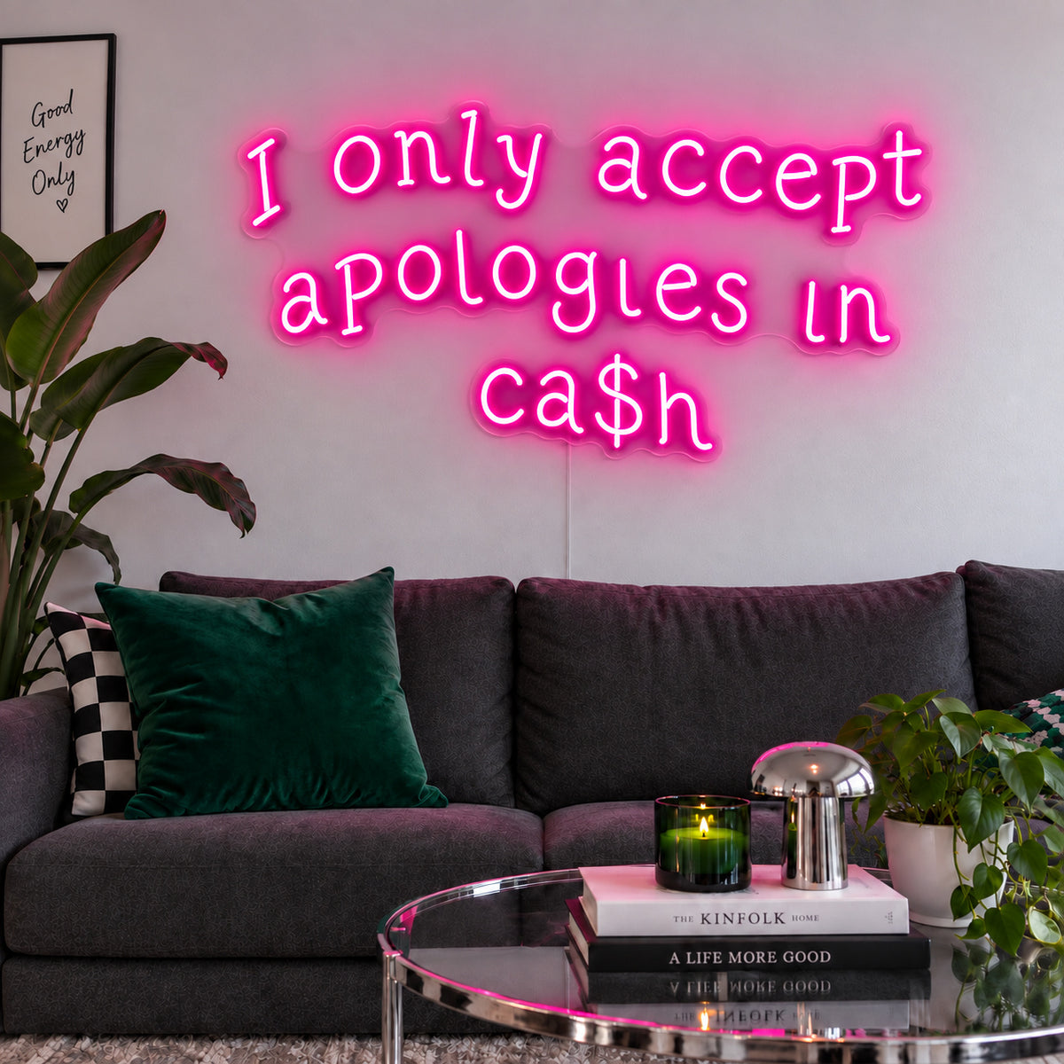 Rose Red version of the I Only Accept Apologies In Ca$h Neon Sign, shown above a charcoal sofa with green cushions.