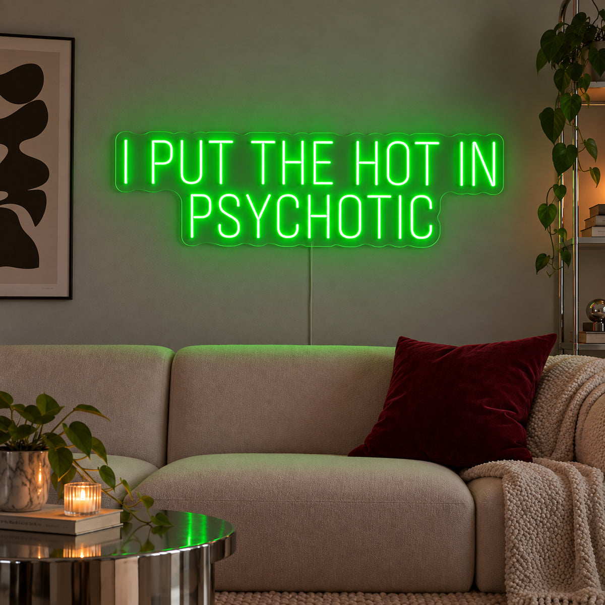 I Put The Hot In Psychotic Neon Sign with green lighting, displayed above a neutral sofa.