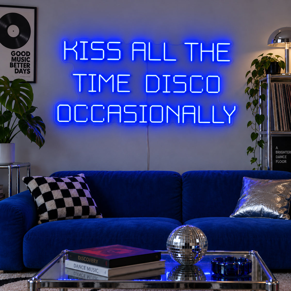 Kiss All The Time Disco Occasionally Neon Sign glowing blue above a blue sofa near a disco ball.