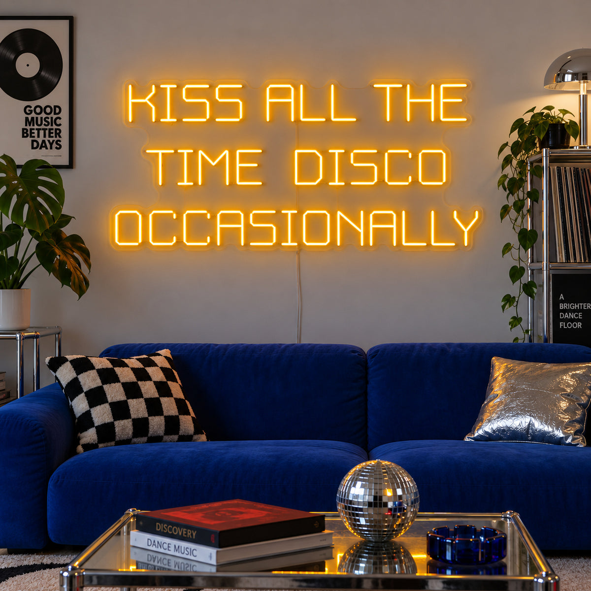 Kiss All The Time Disco Occasionally Neon Sign glowing gold above a blue sofa near a disco ball.