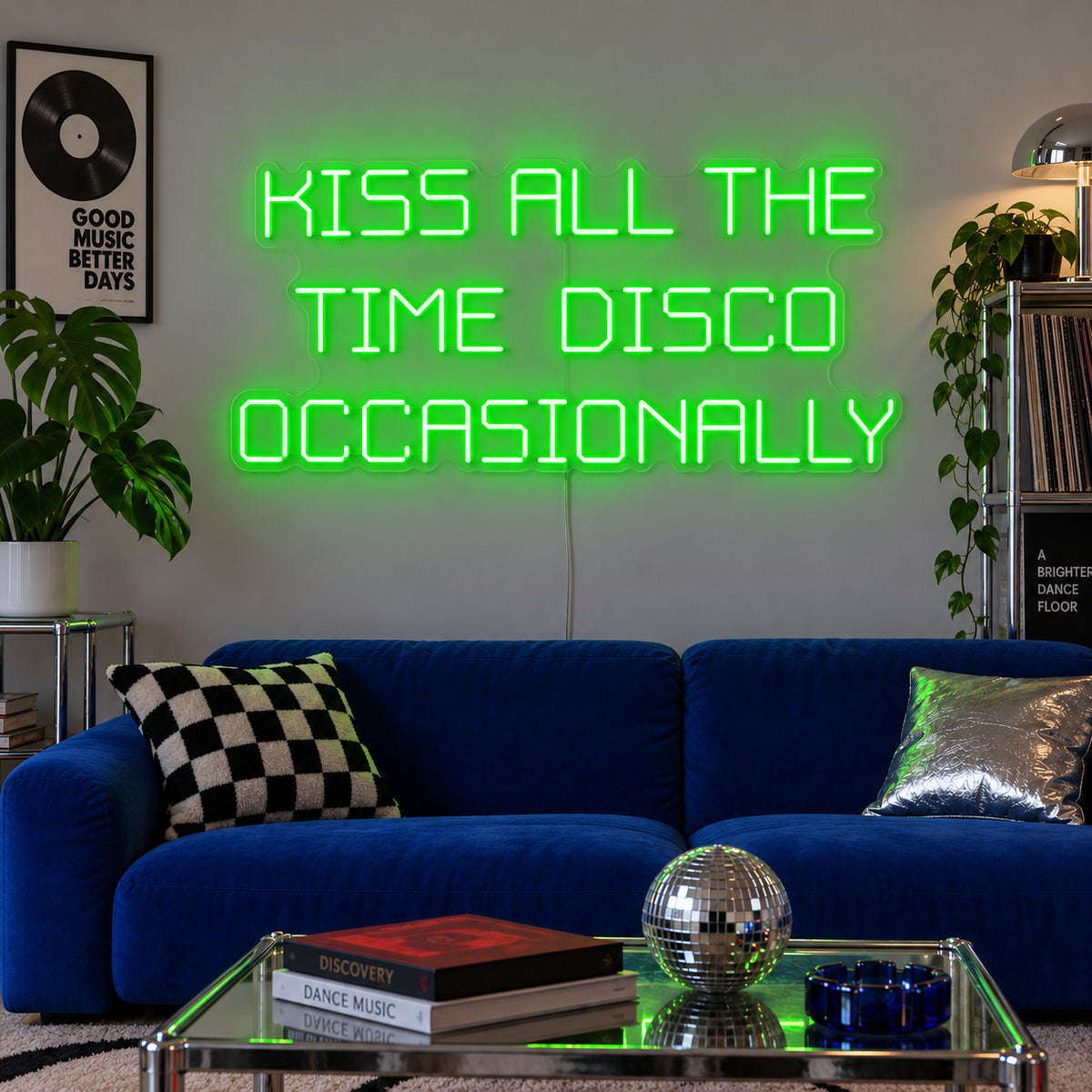 Kiss All The Time Disco Occasionally Neon Sign with green lighting, displayed above a blue sofa near a disco ball.
