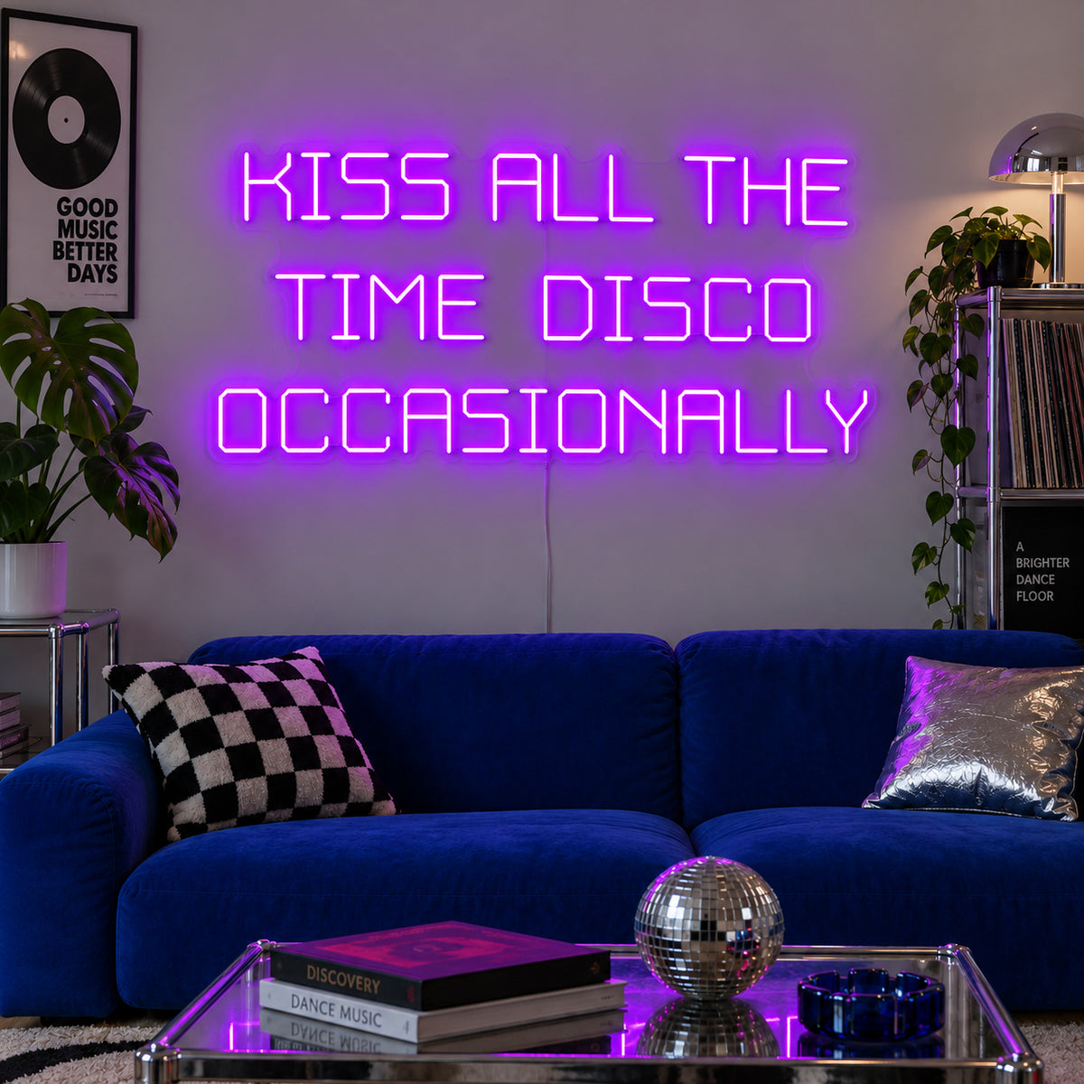 Kiss All The Time Disco Occasionally Neon Sign with purple lighting, displayed above a blue sofa near a disco ball.
