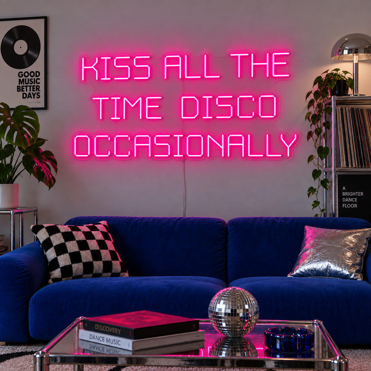Rose Red version of the Kiss All The Time Disco Occasionally Neon Sign, shown above a blue sofa near a disco ball.