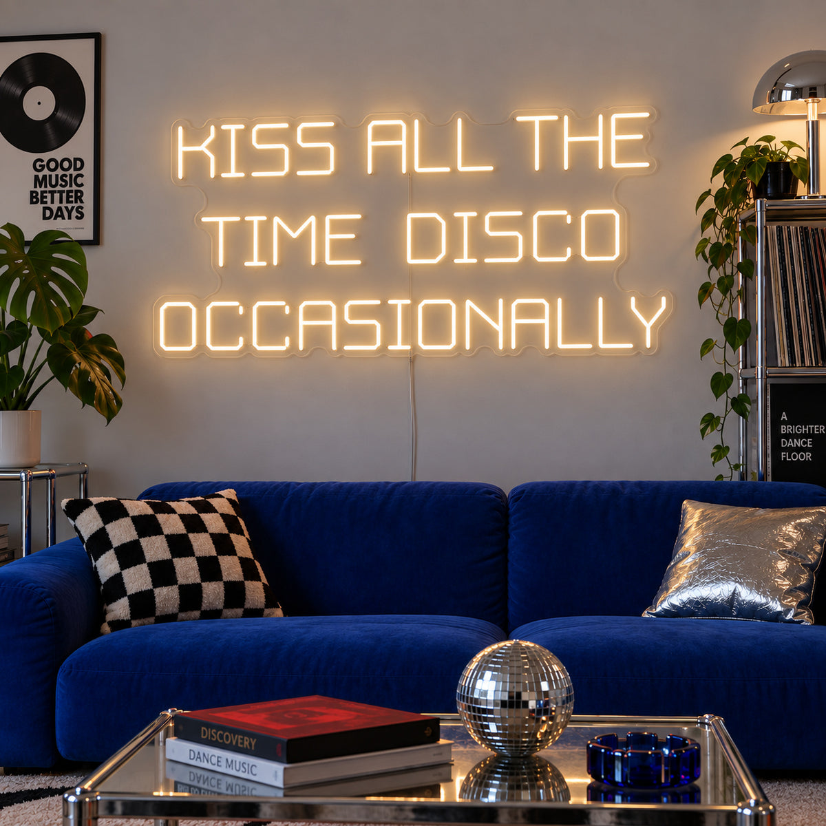 Warm White version of the Kiss All The Time Disco Occasionally Neon Sign, shown above a blue sofa near a disco ball.