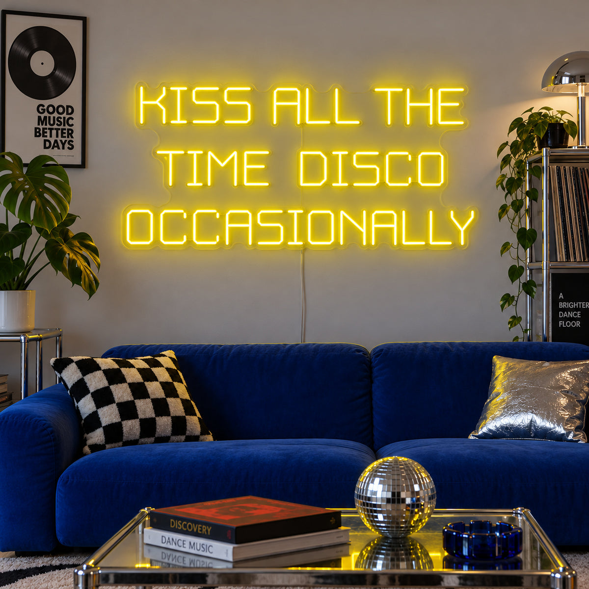Kiss All The Time Disco Occasionally Neon Sign with yellow lighting, displayed above a blue sofa near a disco ball.