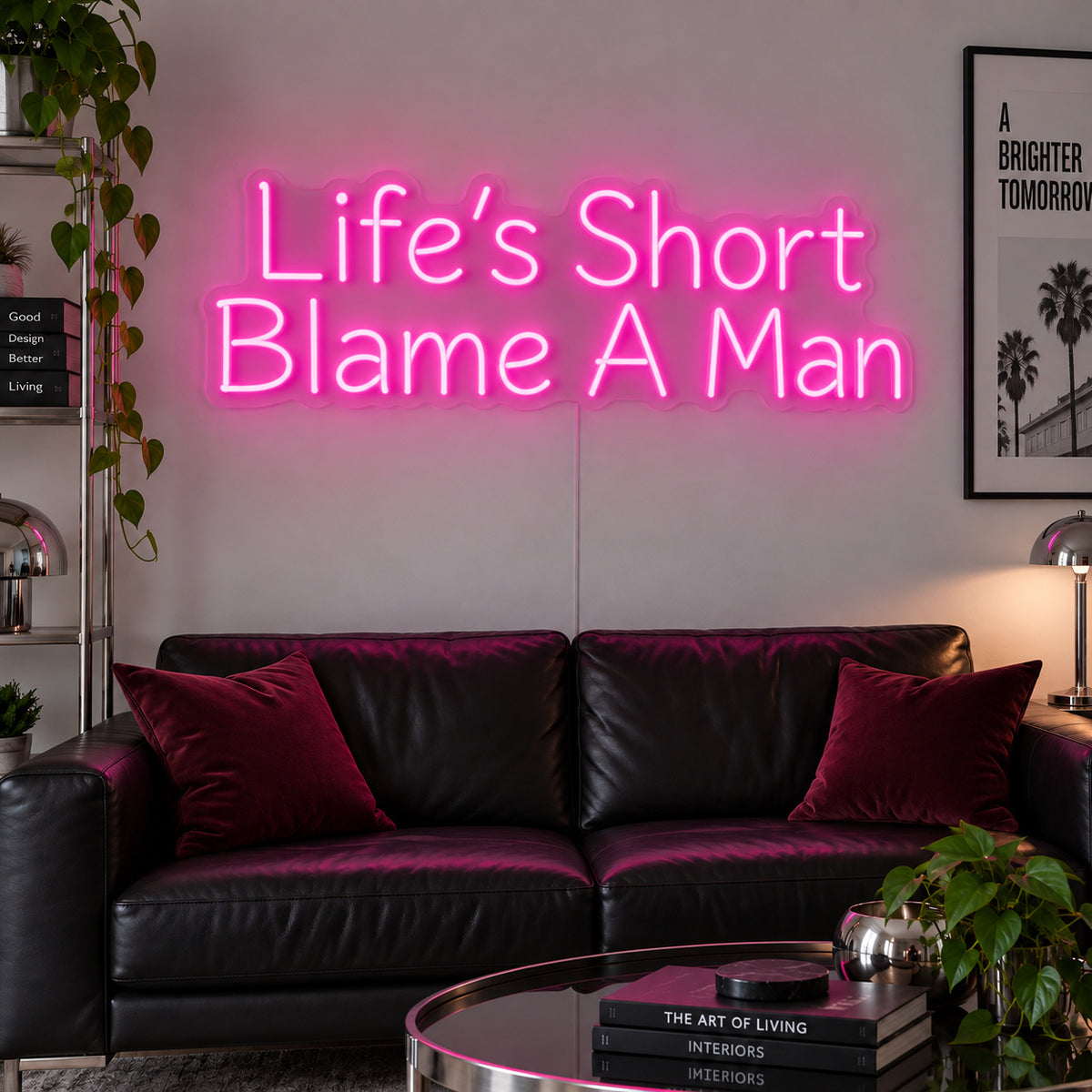 Life's Short Blame A Man Neon Sign glowing pink above a black leather sofa.