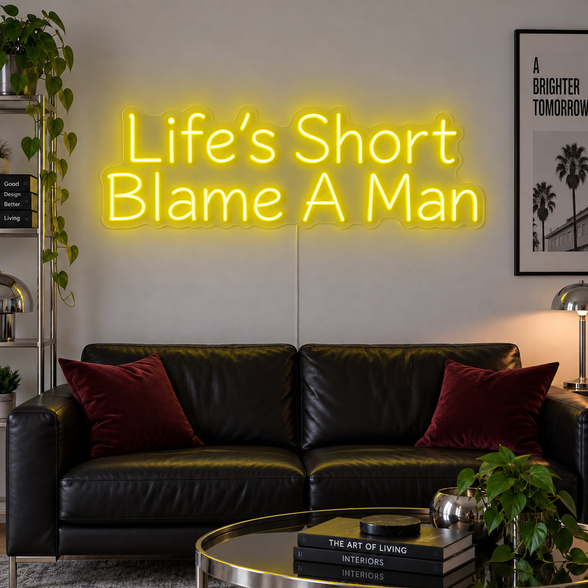 Life's Short Blame A Man Neon Sign with yellow lighting, displayed above a black leather sofa.