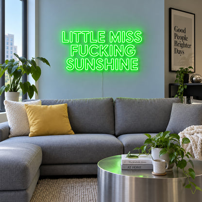 Little Miss Fucking Sunshine Neon Sign with green lighting, displayed above a grey sofa with yellow cushions.