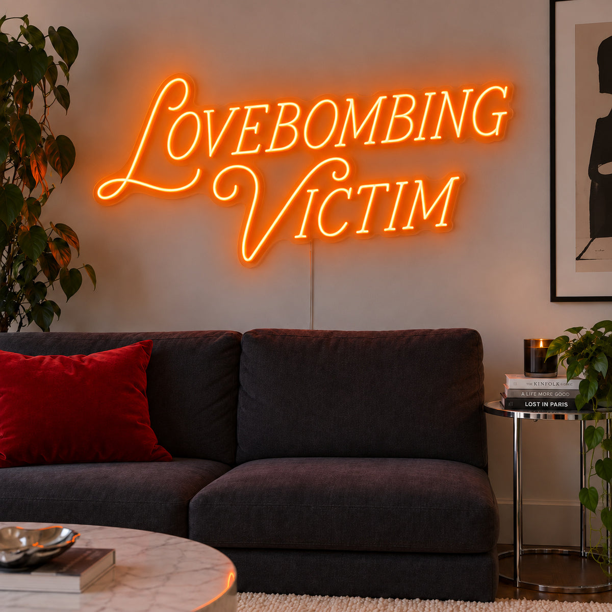 Orange version of the Lovebombing Victim Neon Sign, shown above a dark sofa with red cushions.