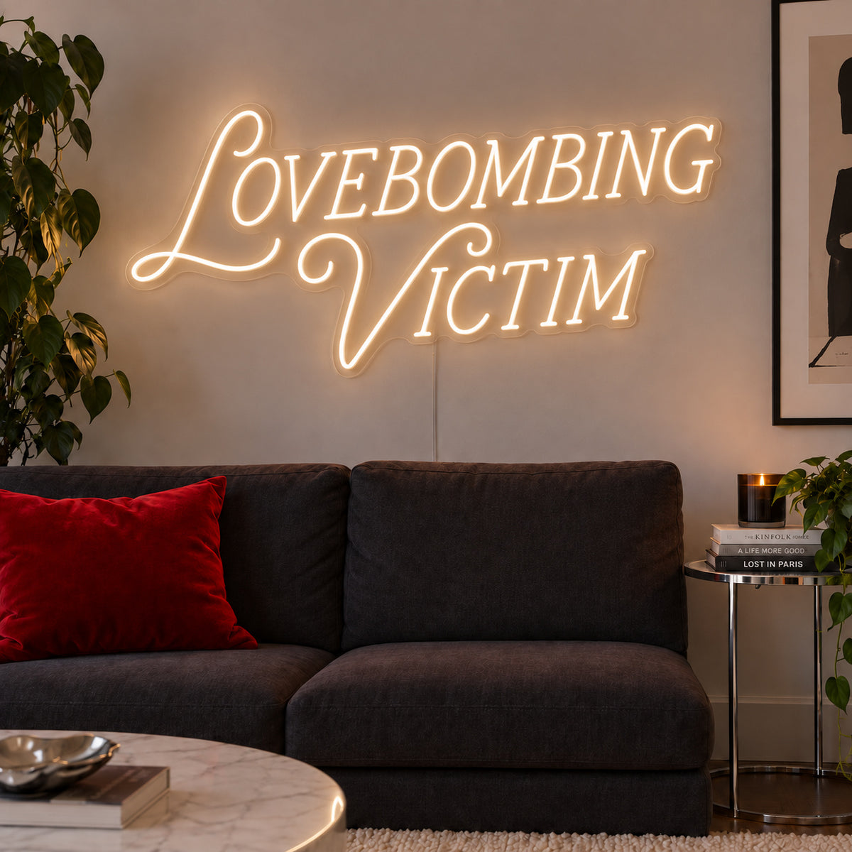 Warm White version of the Lovebombing Victim Neon Sign, shown above a dark sofa with red cushions.