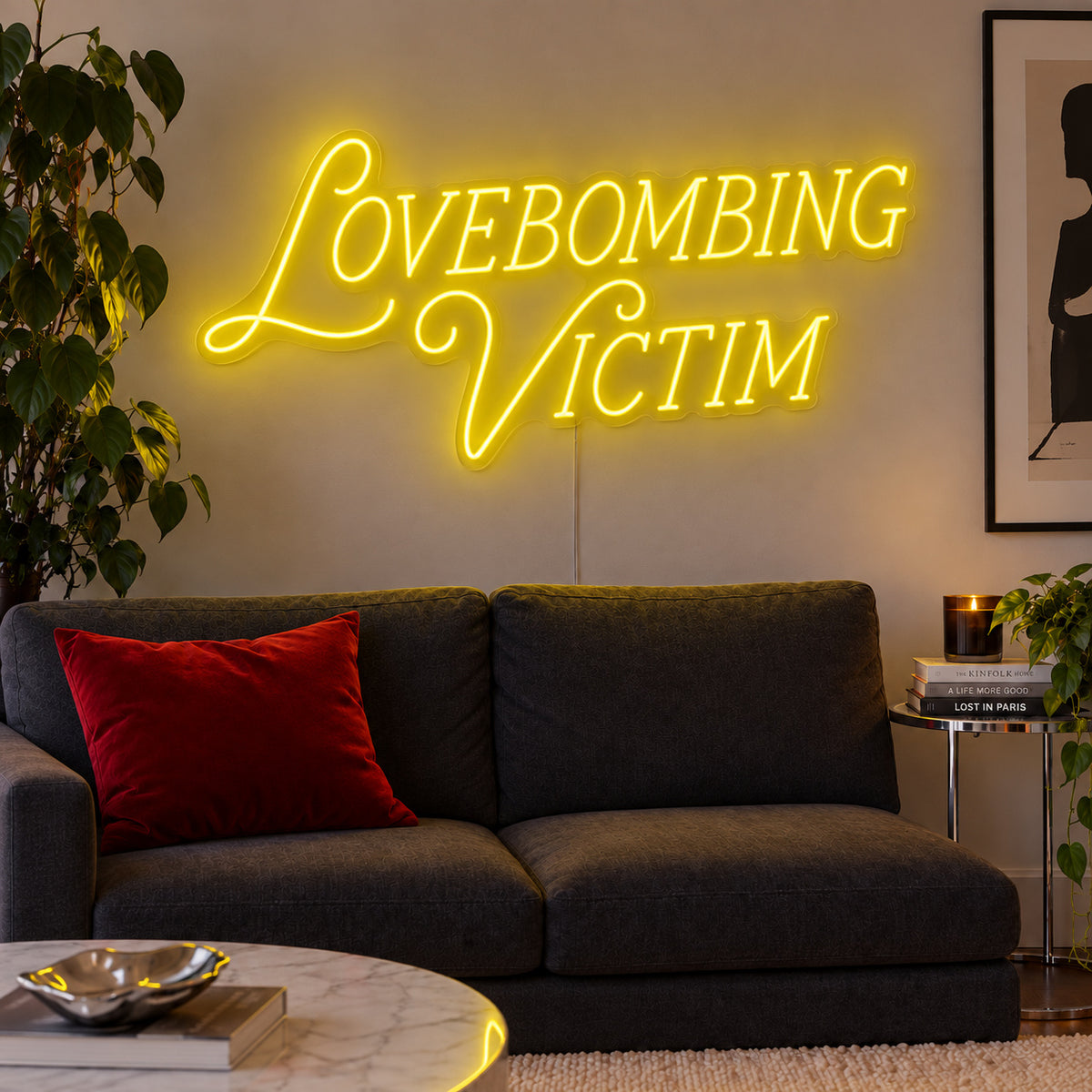 Lovebombing Victim Neon Sign with yellow lighting, displayed above a dark sofa with red cushions.