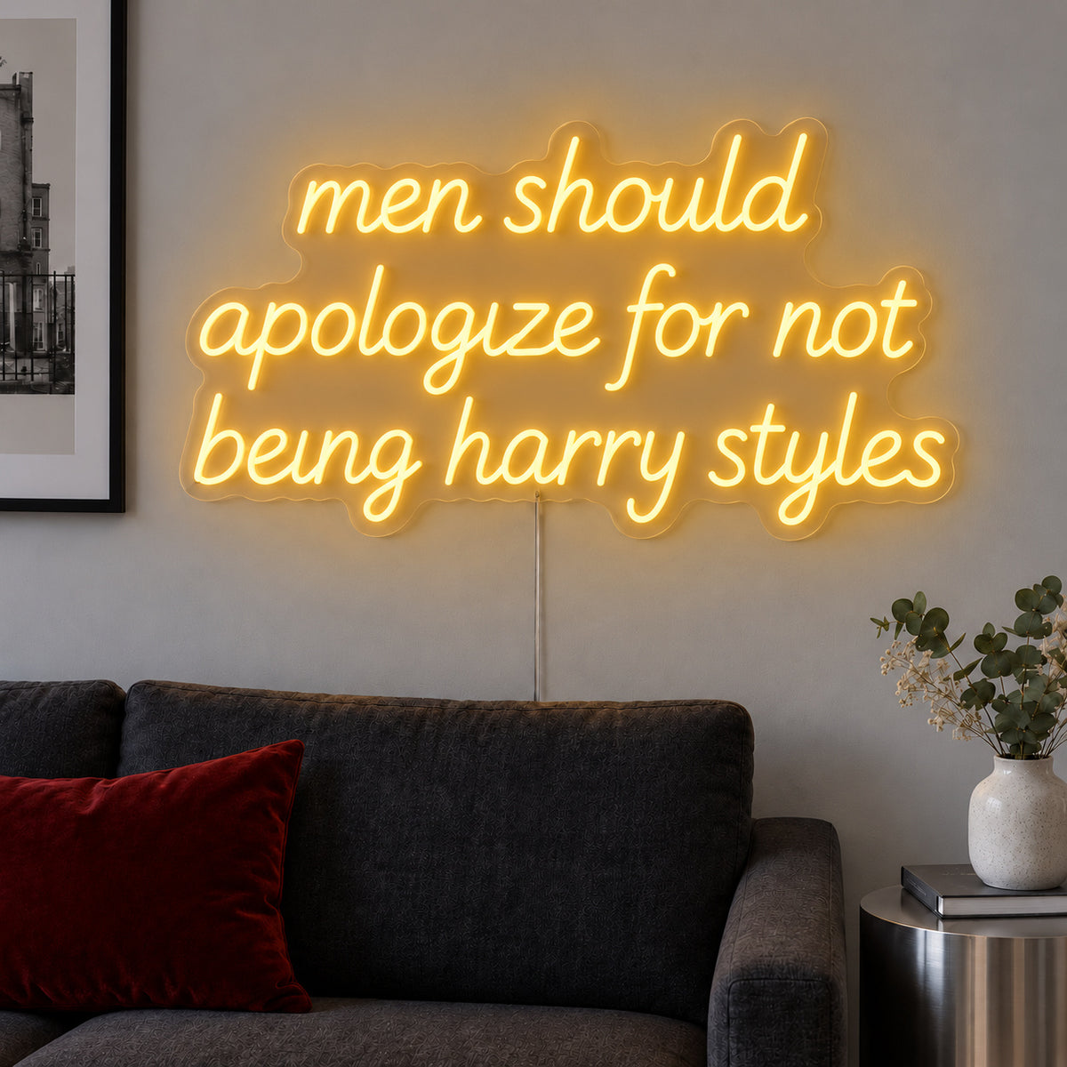 Men Should Apologize For Not Being Harry Styles Neon Sign glowing gold above a dark sofa.