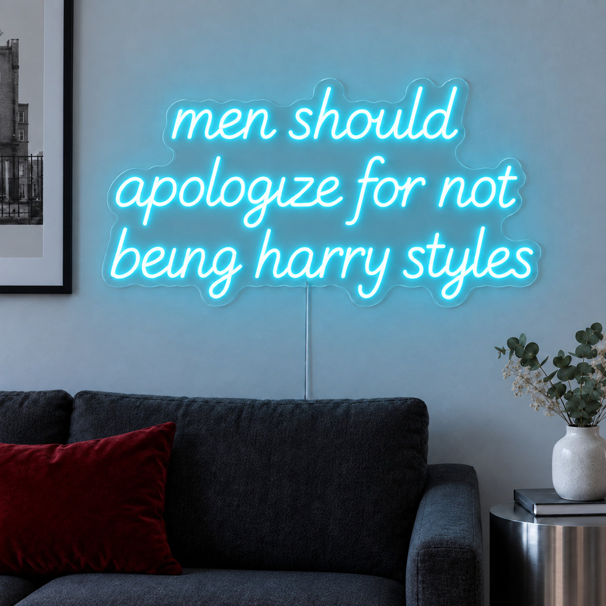 Ice Blue version of the Men Should Apologize For Not Being Harry Styles Neon Sign, shown above a dark sofa.