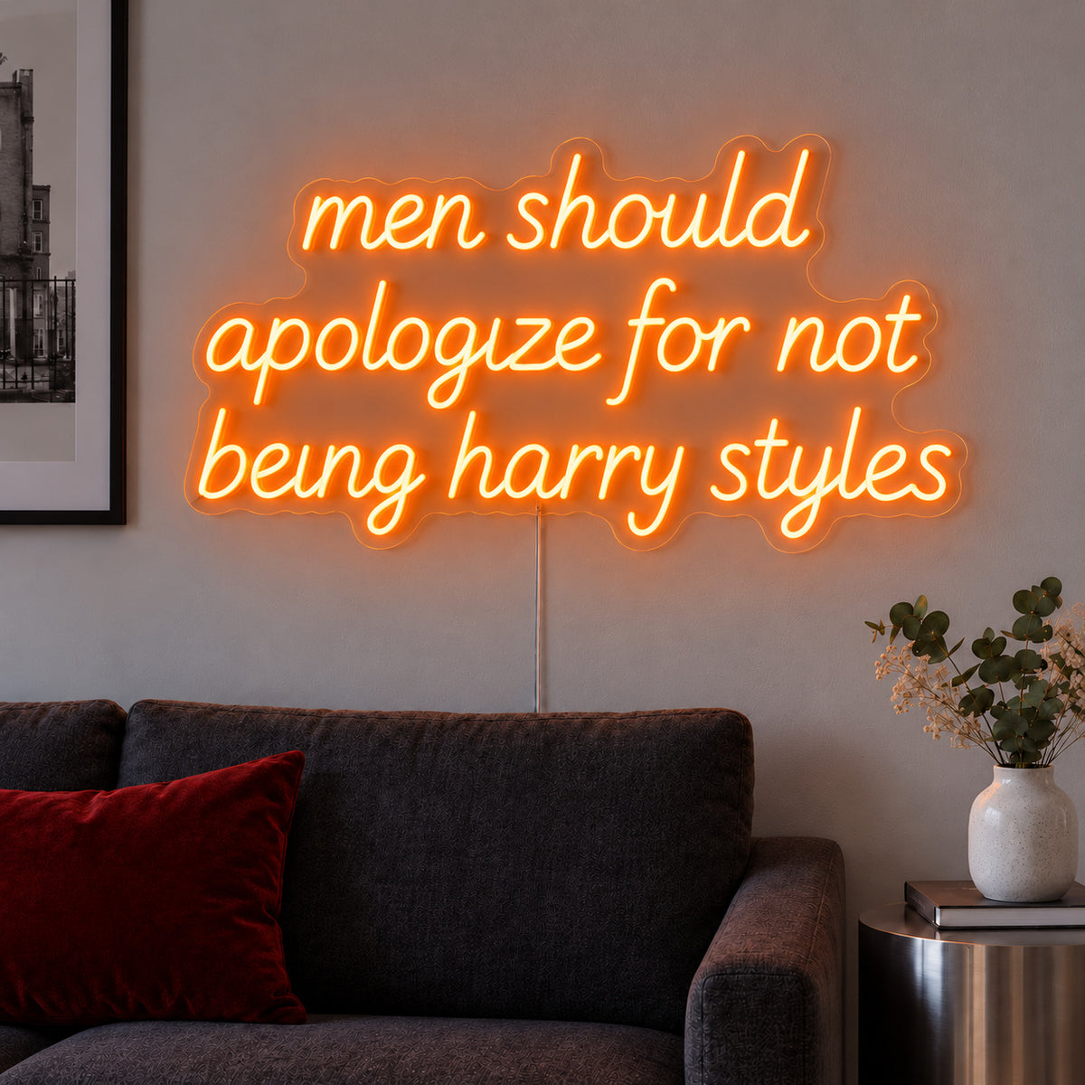 Orange version of the Men Should Apologize For Not Being Harry Styles Neon Sign, shown above a dark sofa.