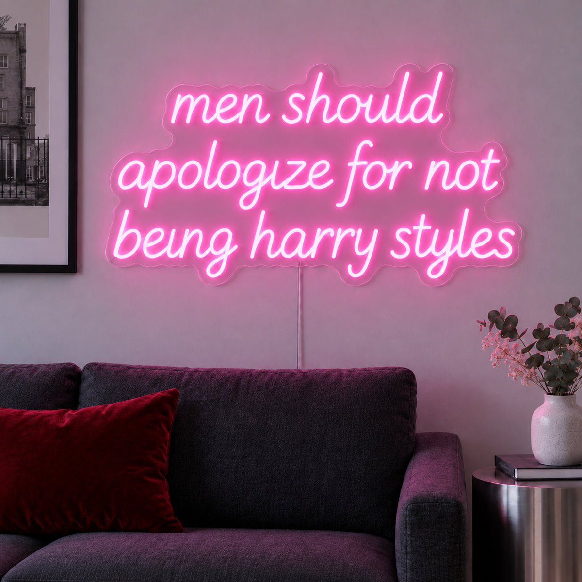 Men Should Apologize For Not Being Harry Styles Neon Sign glowing pink above a dark sofa.