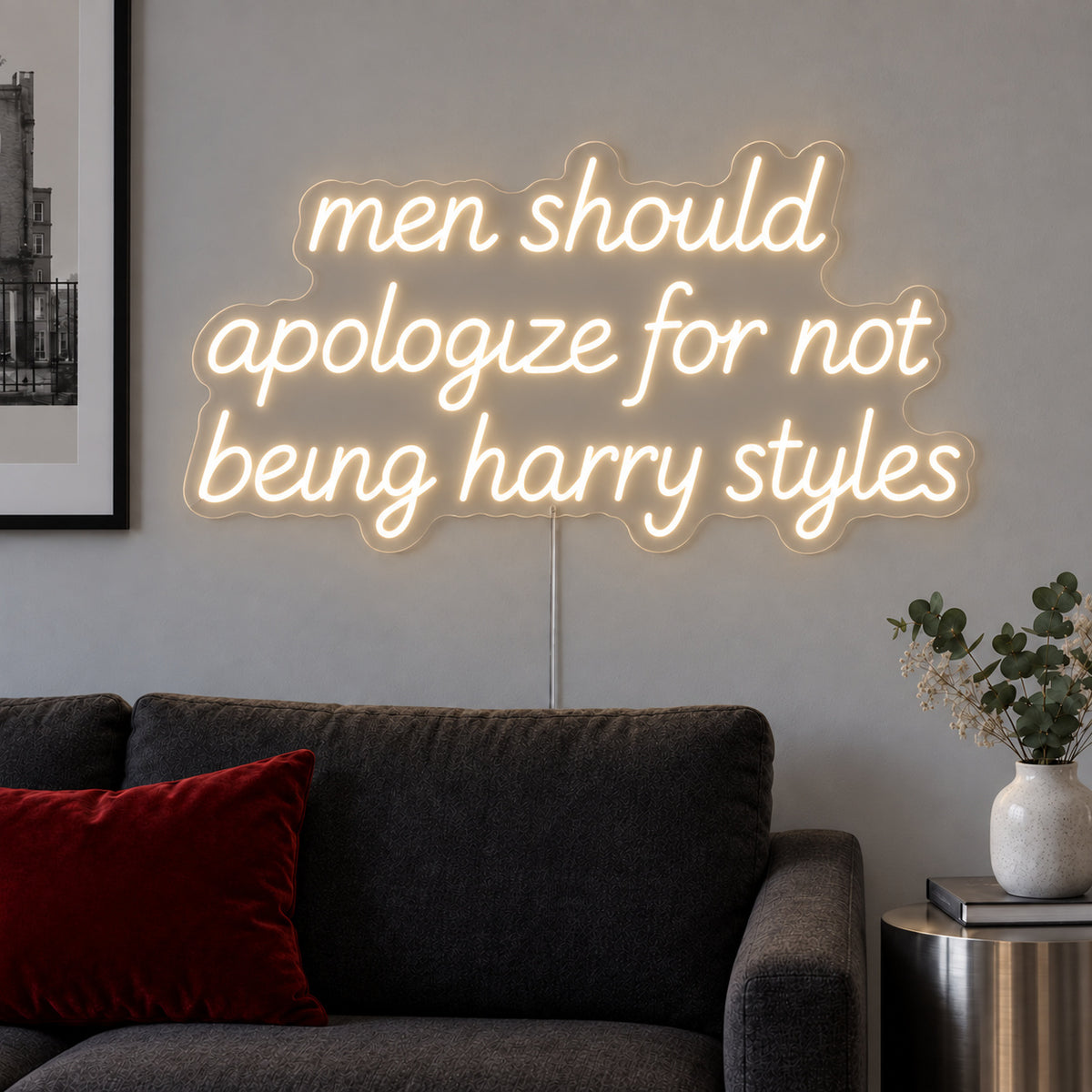 Warm White version of the Men Should Apologize For Not Being Harry Styles Neon Sign, shown above a dark sofa.
