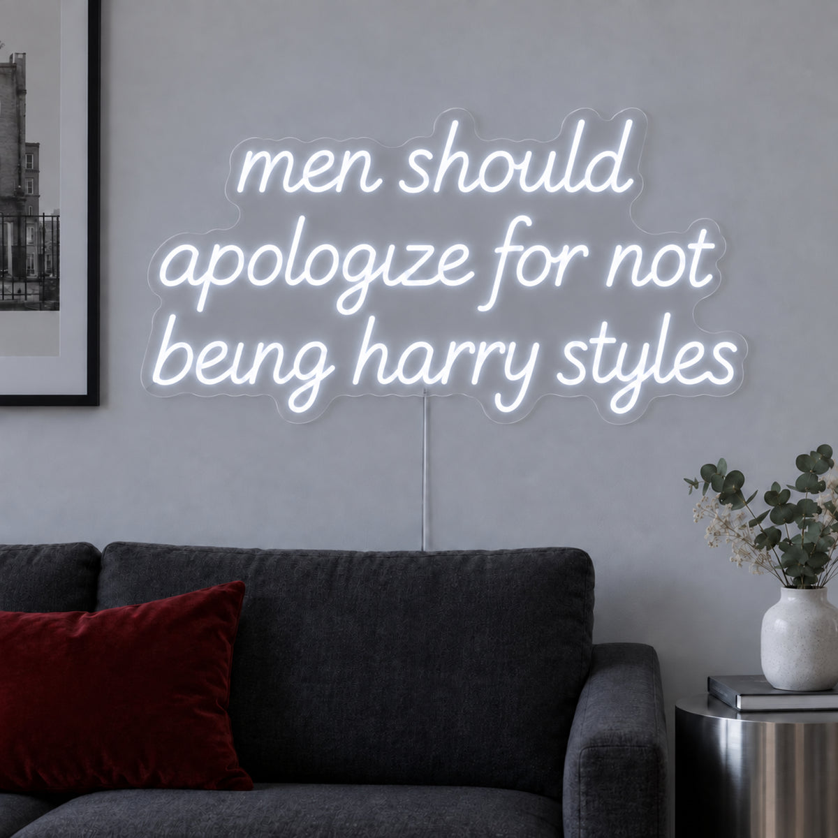 Men Should Apologize For Not Being Harry Styles Neon Sign in white above a dark sofa.