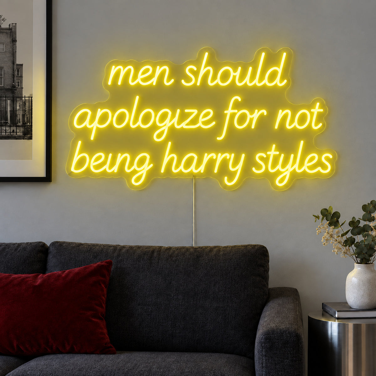 Men Should Apologize For Not Being Harry Styles Neon Sign with yellow lighting, displayed above a dark sofa.