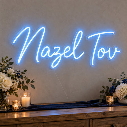 Mazel Tov Blue Neon Sign on clear cut-to-shape acrylic, illuminated on a wall in a styled celebration setting
