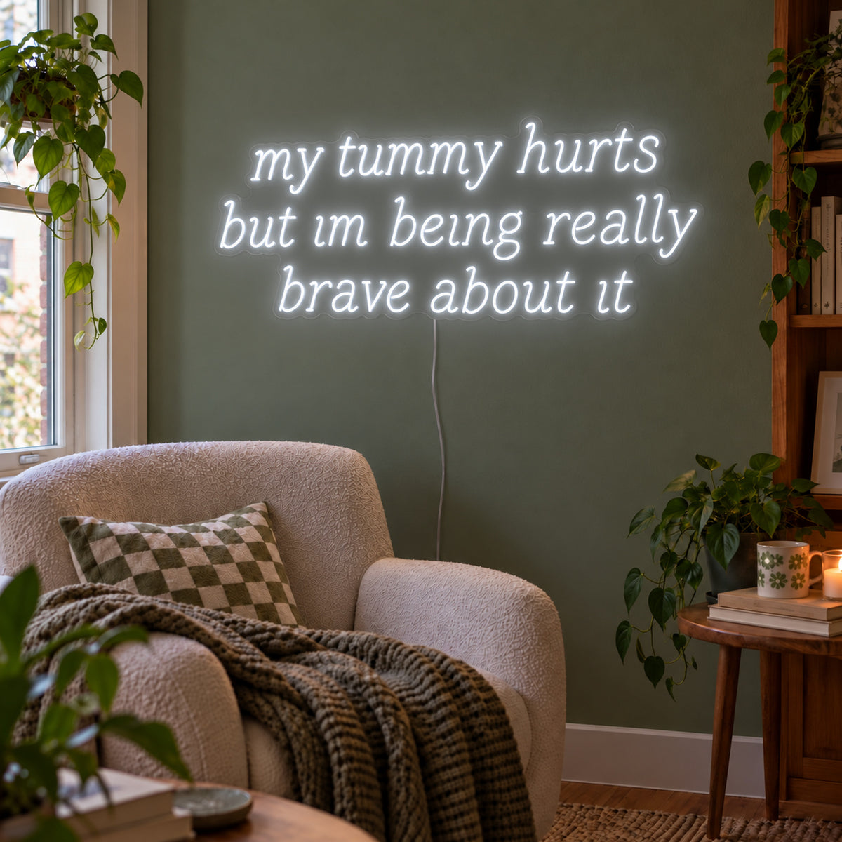 My Tummy Hurts But Im Being Really Brave About It Neon Sign, RGB colour-changing option shown in white above a reading chair against a green wall.