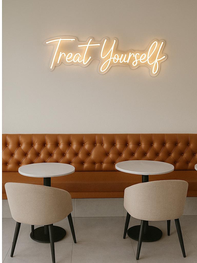 Neon sign reading 'Treat Yourself' above a brown leather booth with white tables and chairs.