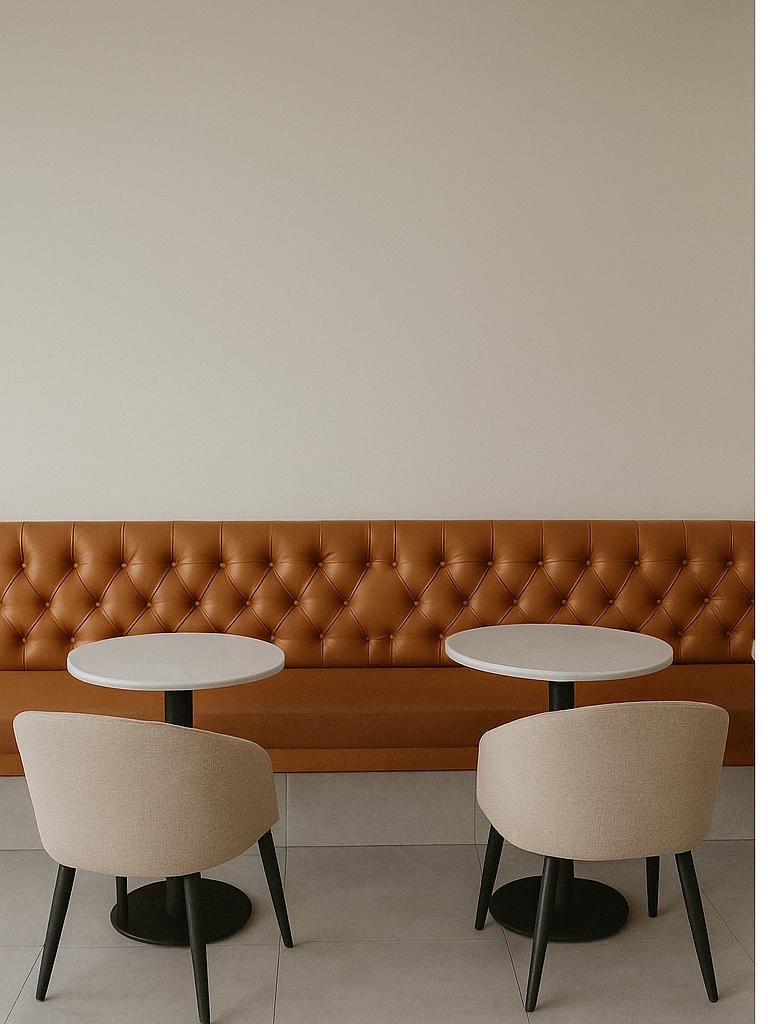 Two round tables with chairs in front of a brown leather bench against a beige wall.