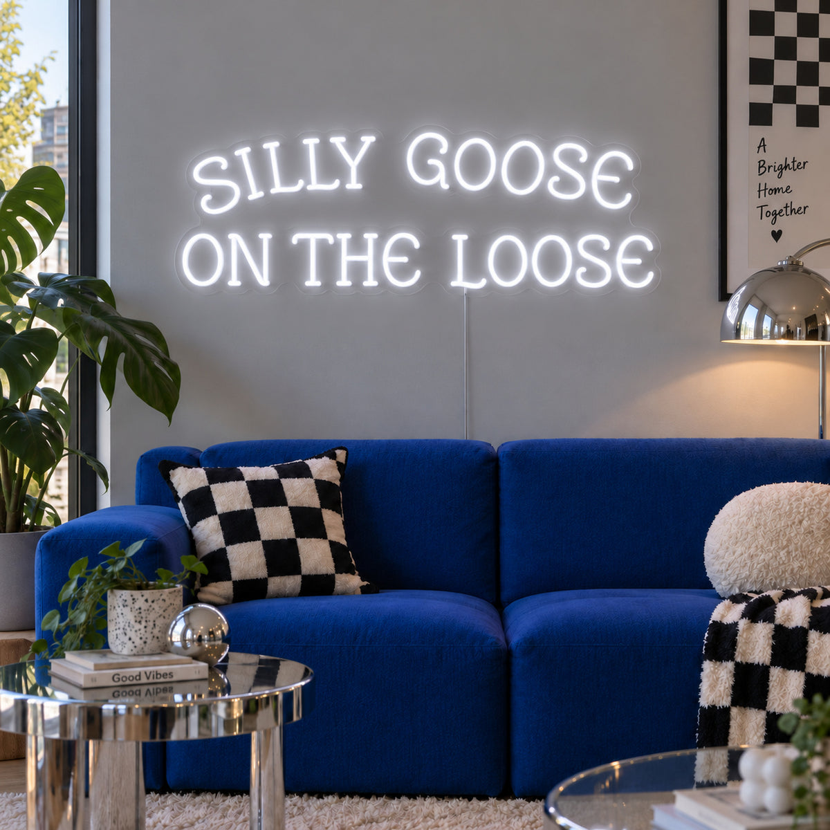 Silly Goose On The Loose Neon Sign glowing white above a blue sofa with checkered cushions.