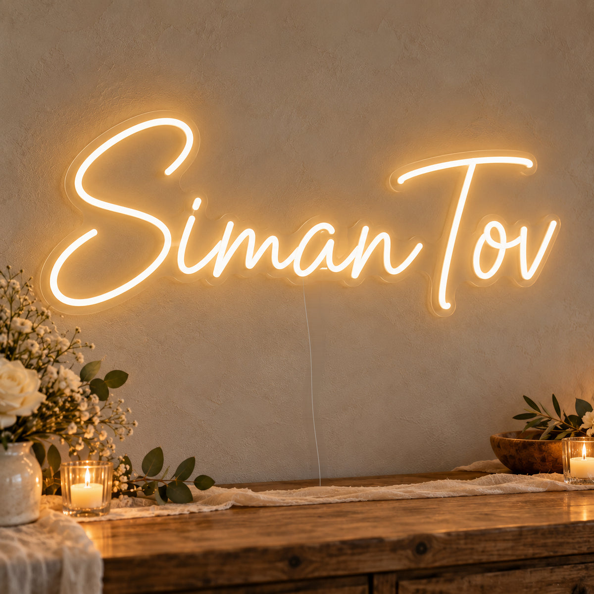 Siman Tov Neon Sign on clear cut-to-shape acrylic, illuminated on a wall in a styled celebration setting