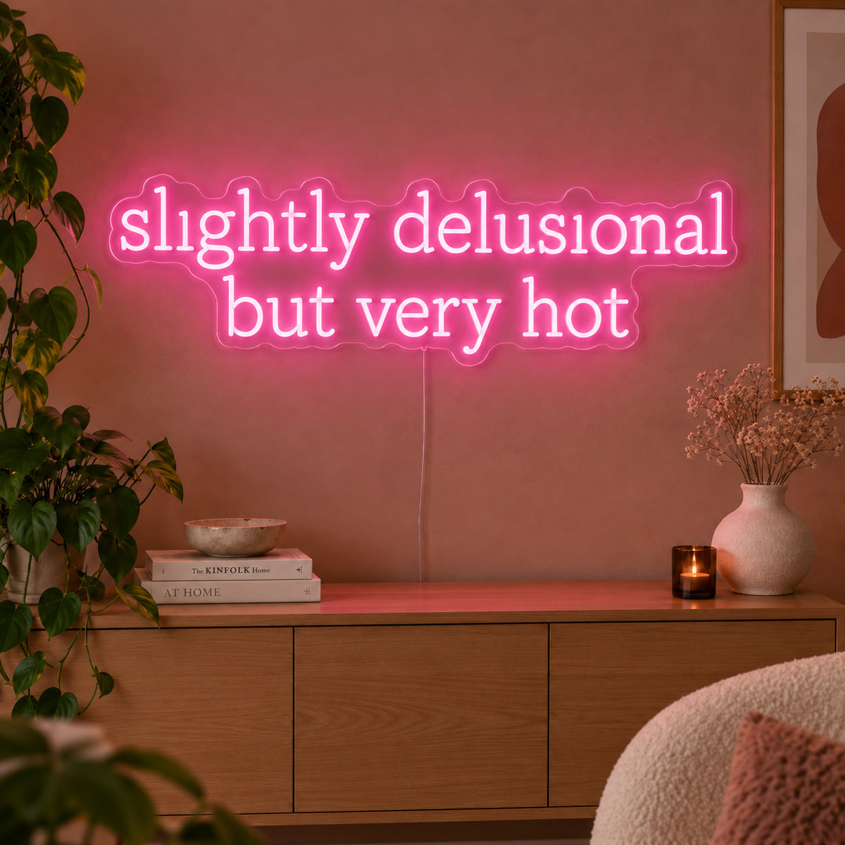 Slightly Delusional But Very Hot Neon Sign glowing pink above a wooden sideboard.