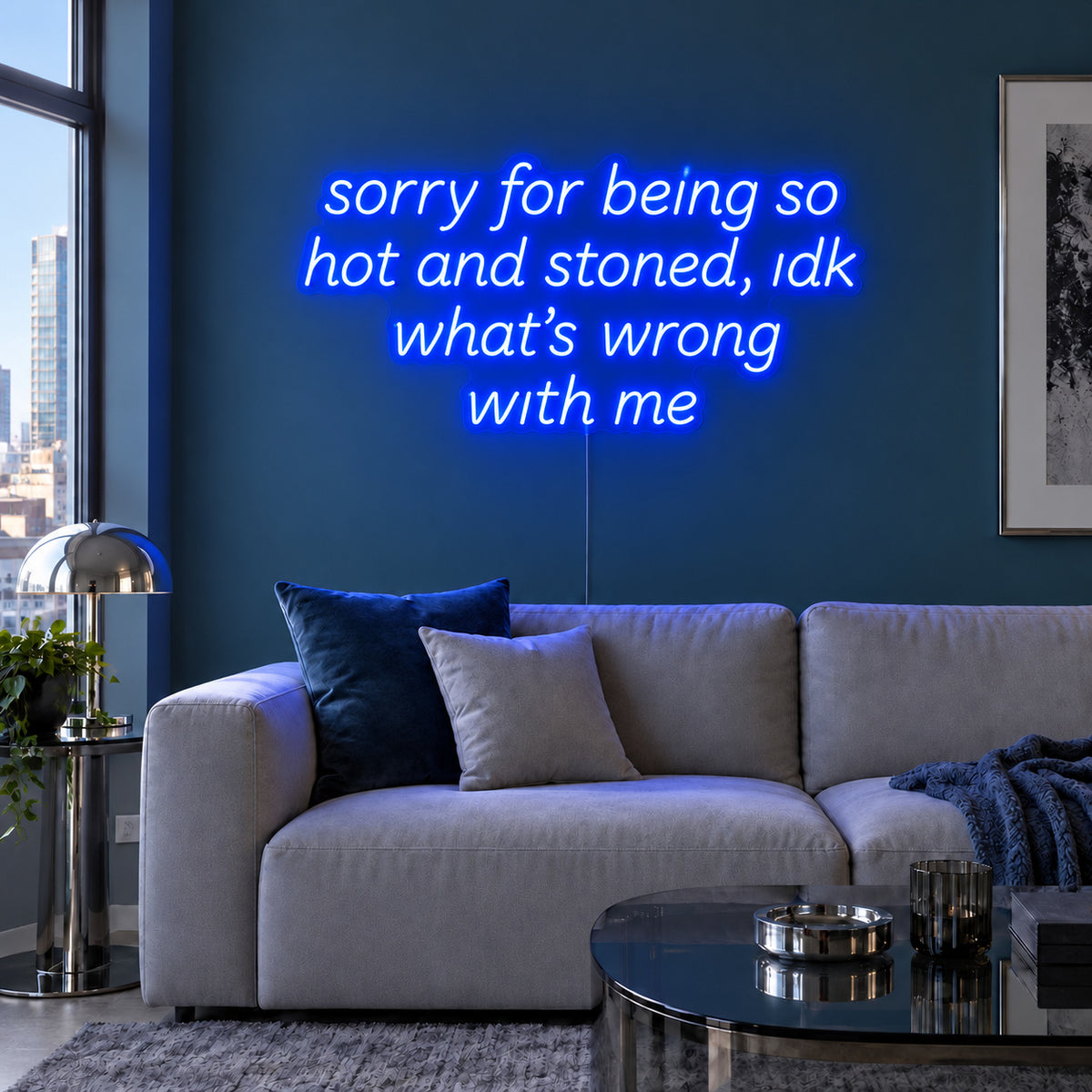 Sorry For Being So Hot And Stoned, Idk What's Wrong With Me Neon Sign glowing blue above a grey sofa against a blue wall.