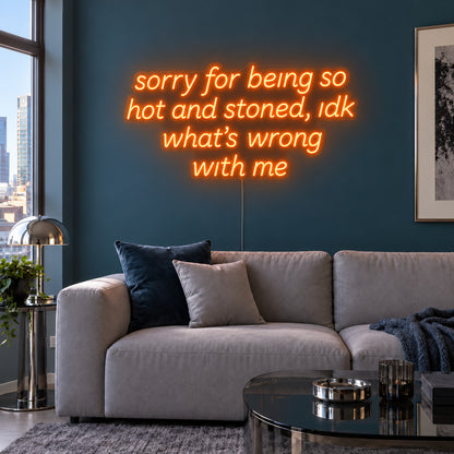 Orange version of the Sorry For Being So Hot And Stoned, Idk What's Wrong With Me Neon Sign, shown above a grey sofa against a blue wall.