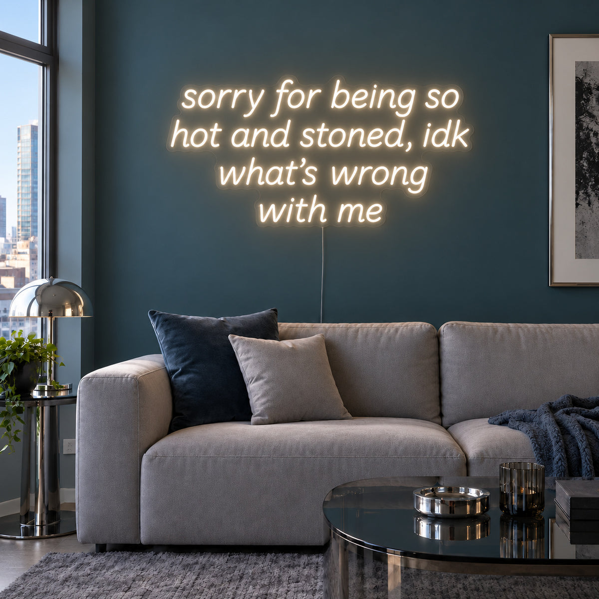 Warm White version of the Sorry For Being So Hot And Stoned, Idk What's Wrong With Me Neon Sign, shown above a grey sofa against a blue wall.