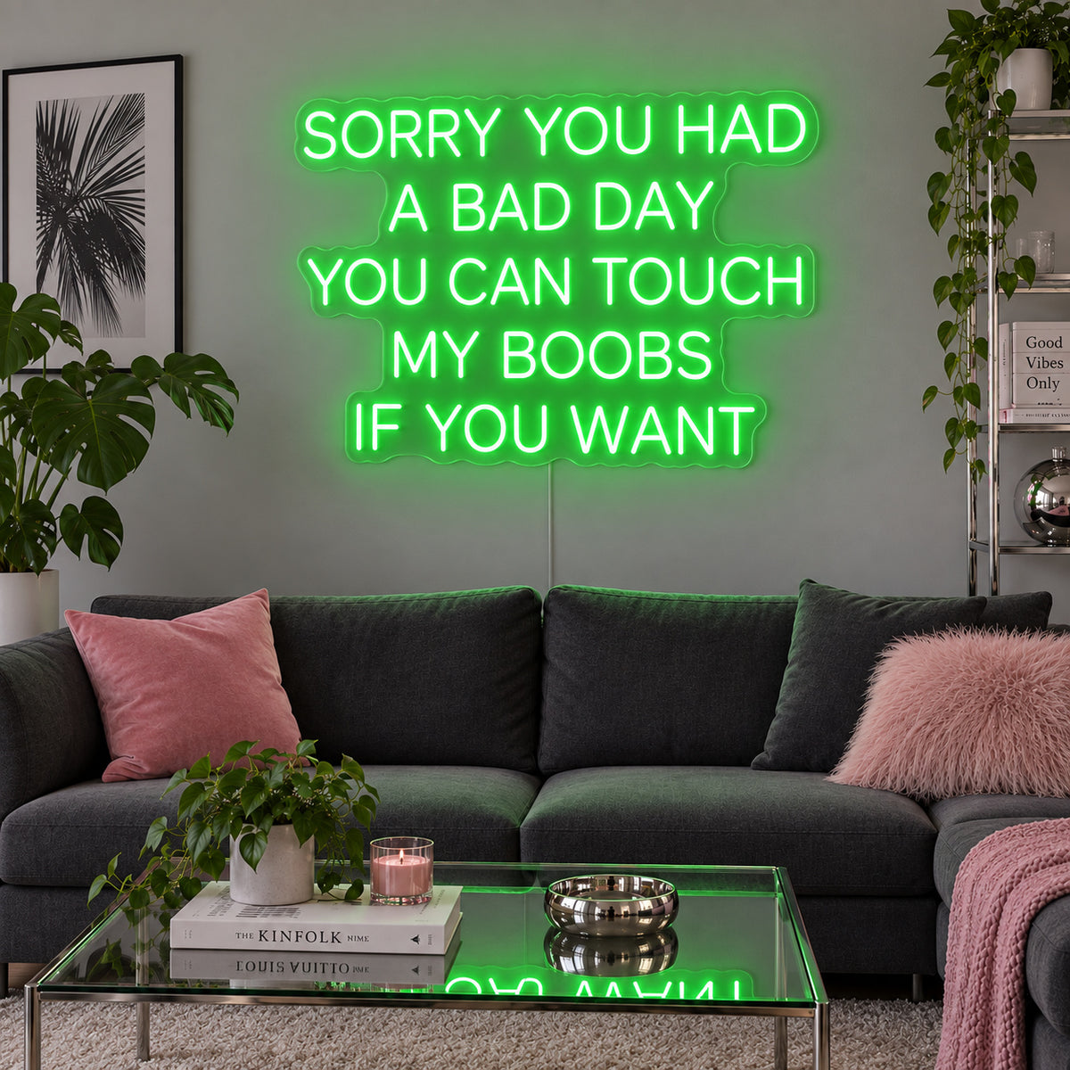 Sorry You Had A Bad Day You Can Touch My Boobs If You Want Neon Sign with green lighting, displayed above a grey sofa with pink cushions.
