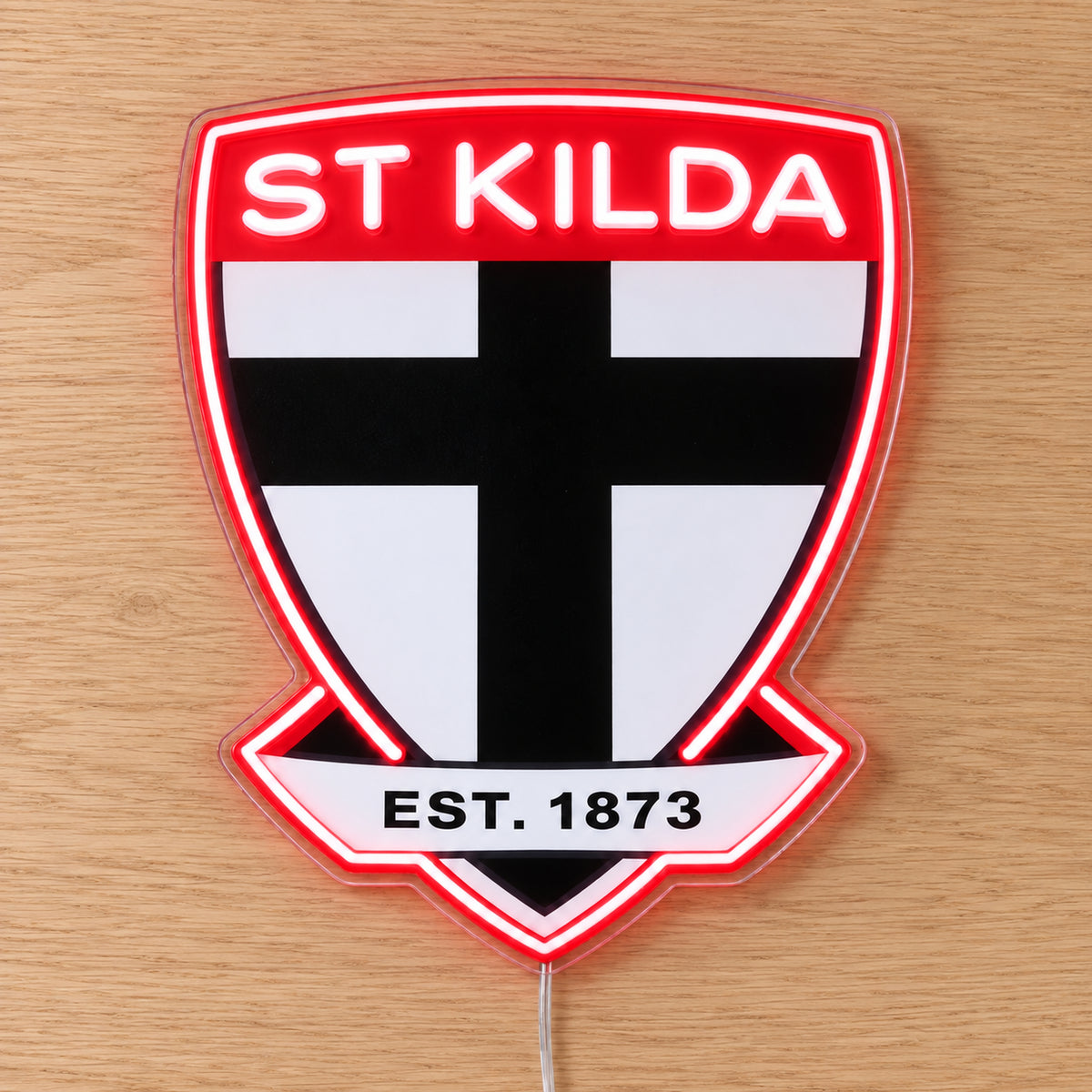 St Kilda Saints Neon Sign with white neon lettering and red outline, lying flat on light wood